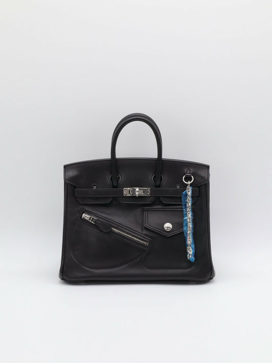Black leather Birkin-style handbag with palladium hardware, zip pocket and snap flap pocket on the front, chain charm attached