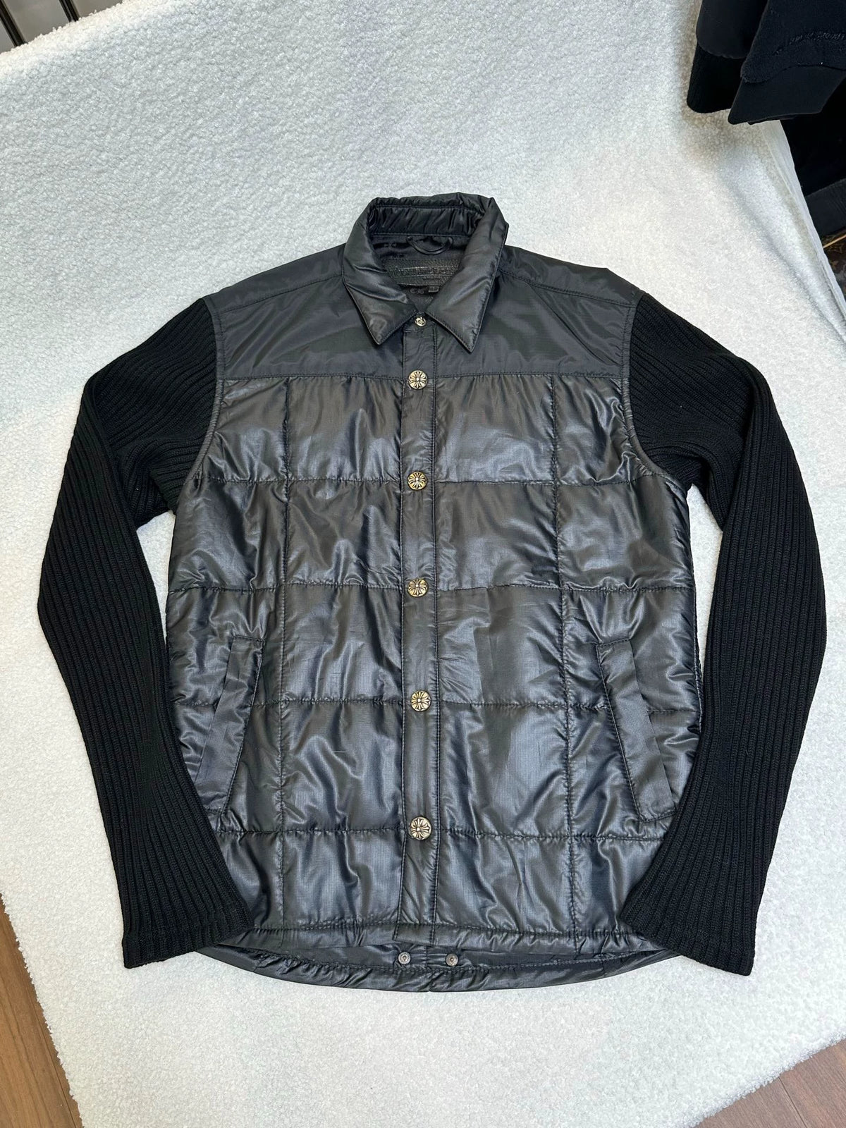 Black quilted jacket with ribbed knit sleeves, nylon body, silver cross-motif snap buttons and a shirt collar
