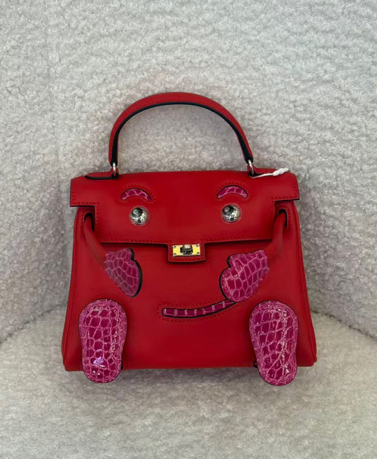 Red leather top-handle bag with face design, magenta crocodile-embossed cheeks, feet and smile, silver eyes and gold turn-lock