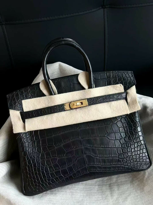 Black matte crocodile-embossed top-handle handbag with gold-tone turn-lock hardware, twin rolled handles and cream felt protector